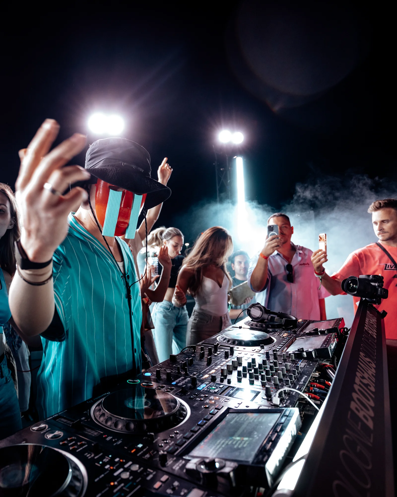 DHALI am DJ-Pult, umgeben von Publikum und hellem Bühnenlicht