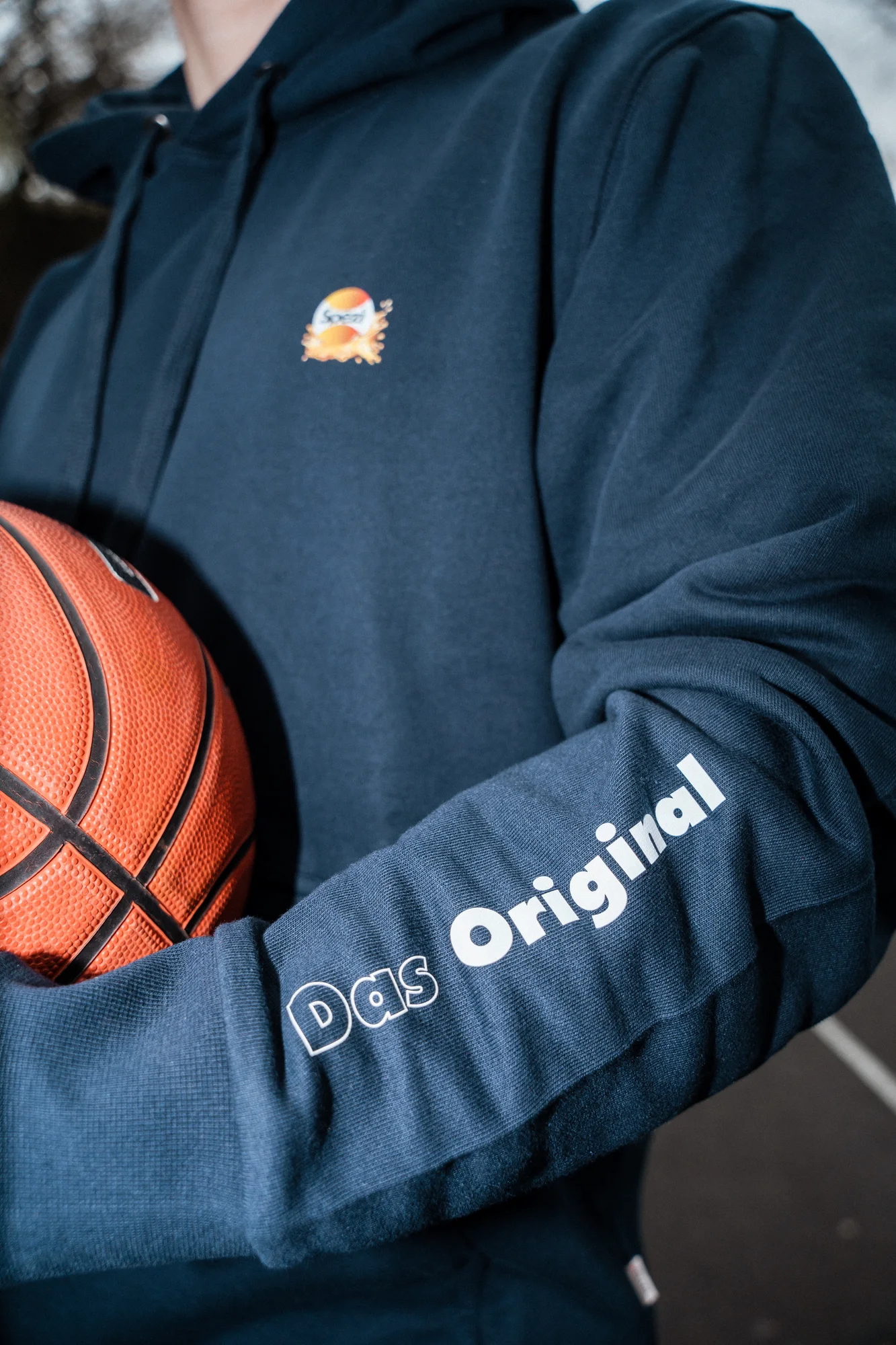Detail des Spezi-Merch-Hoodies mit Logo, Ärmelaufdruck und Basketball