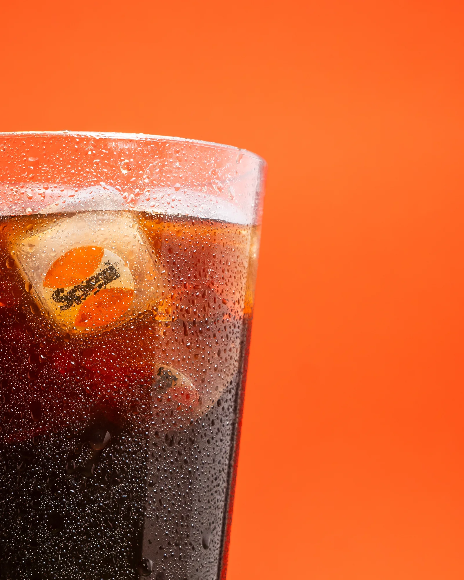 Spezi im Glas mit Wassertropfen vor kräftigem Orange