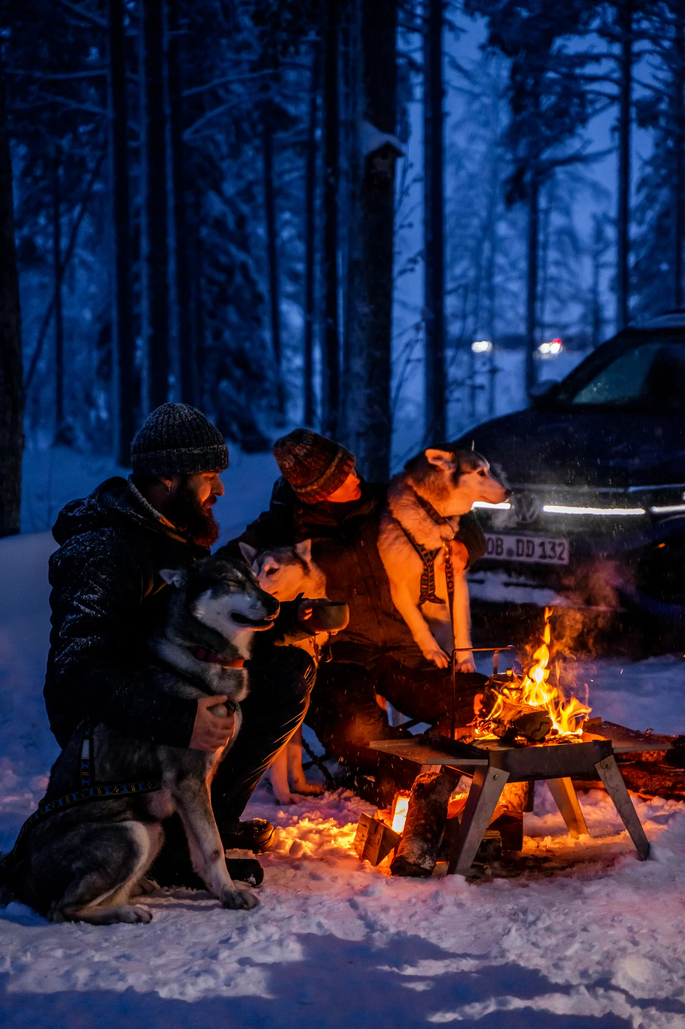 Menschen und Huskys am Lagerfeuer mit Volkswagen im Hintergrund