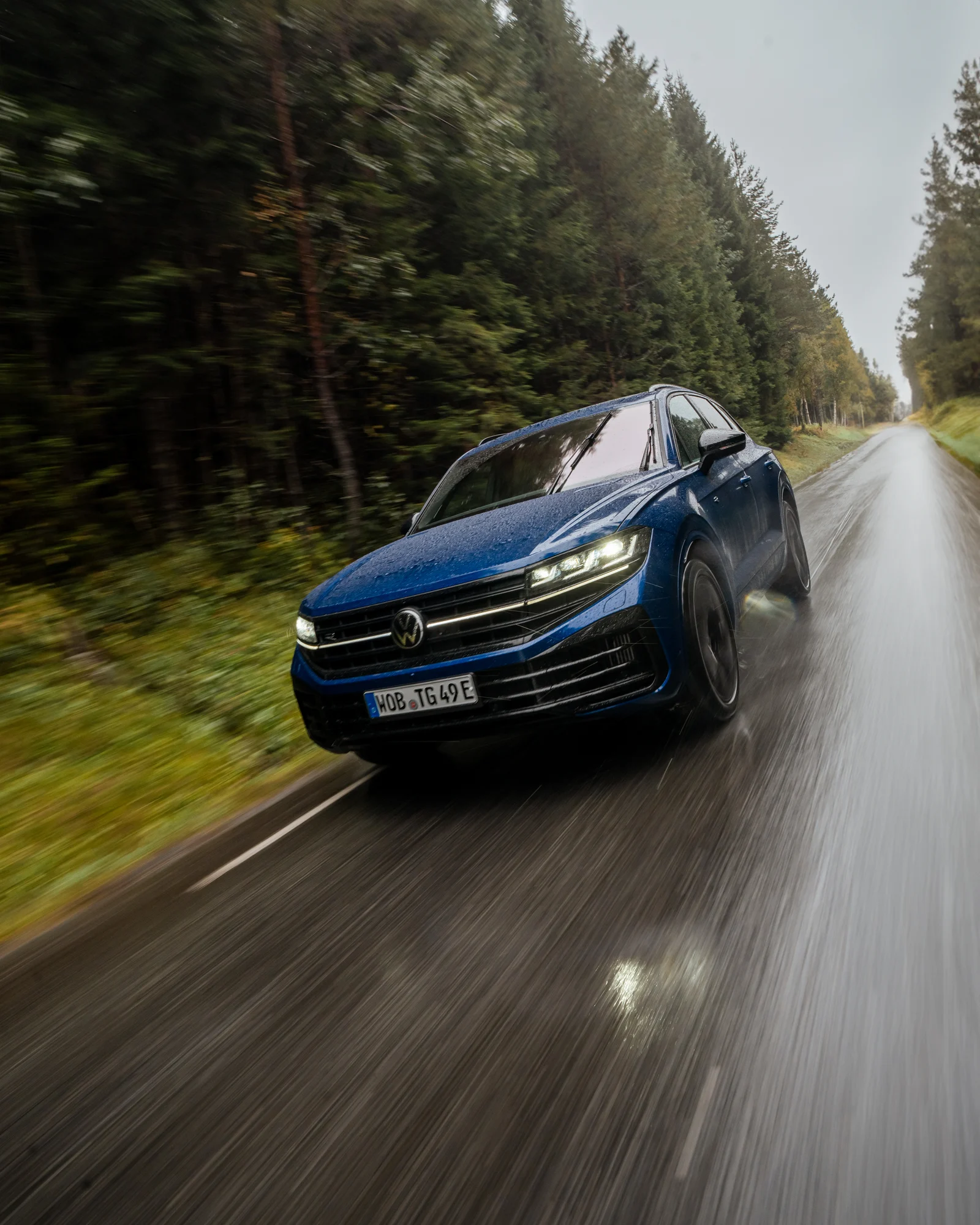 Blauer Volkswagen in Fahrt auf einer nassen Waldstraße
